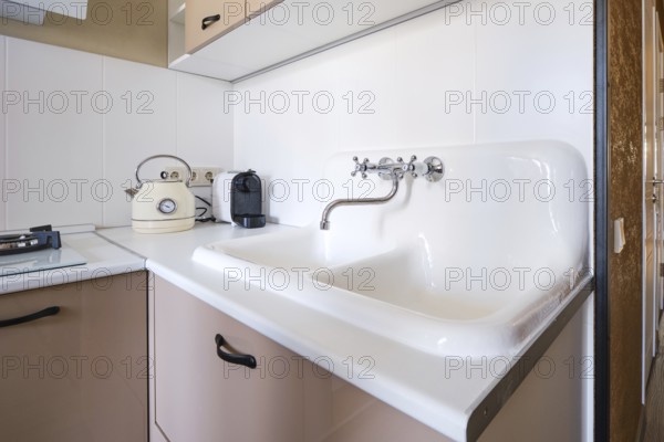 A clean kitchen space features a double sink with a vintage kettle beside a sleek coffee maker. Sunlight brightens the area, highlighting the minimalist design and functional layout
