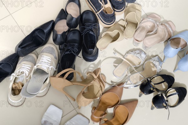 A collection of diverse footwear types is arranged on a light-colored tiled floor. Styles include sneakers, sandals, heels, and flats, showcasing different colors and designs in a playful manner