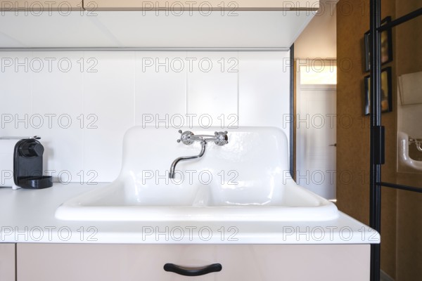 An old-fashioned white sink with a chrome faucet on a countertop in a modern kitchen. The space is well-lit, showcasing kitchen appliances and a minimalist design