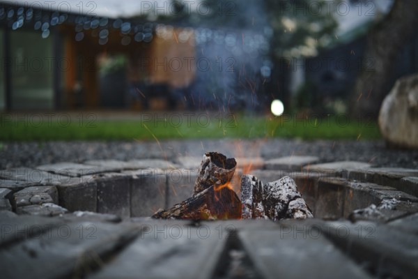 A fire pit crackles with bright flames and glowing embers, surrounded by rustic stones