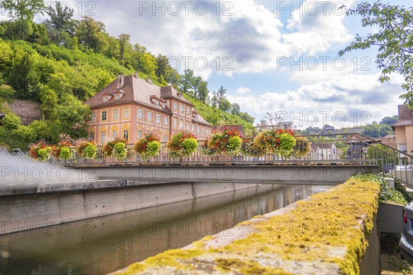 Historic building by the river, surrounded by blooming flowers and a green hill, small town pearl Calw, Black Forest, Germany