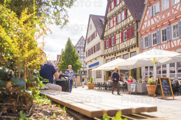 Cosy street scene with half-timbered houses and cafés under parasols on a sunny day, small town pearl Calw, Black Forest, Germany