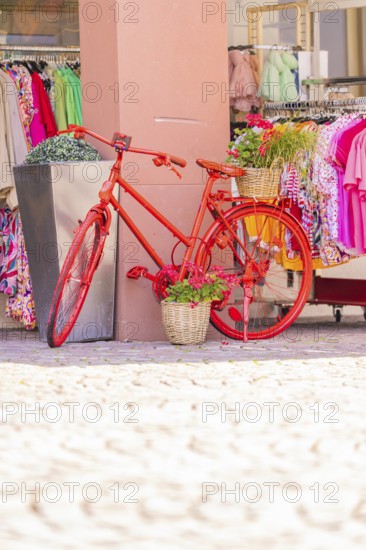 Red bicycle decoratively in front of a clothing shop, surrounded by colourful clothes, small town of Perle Calw, Black Forest, Germany