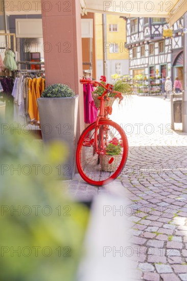A bicycle with red flower baskets stands in front of half-timbered houses and shops in a town, small town pearl Calw, Black Forest, Germany