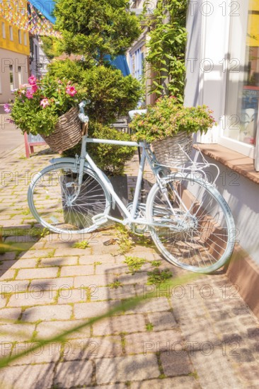 Pale bicycle with lush flower baskets on a sunny street, small town of Perle Calw, district of Calw, Germany