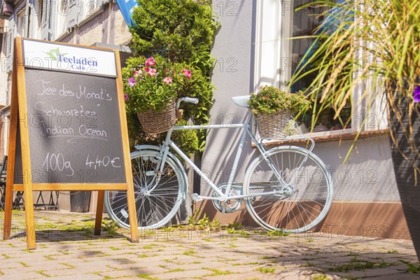 A pale bicycle with flowers in baskets next to a chalkboard in front of a café, small town of Perle Calw, district of Calw, Germany