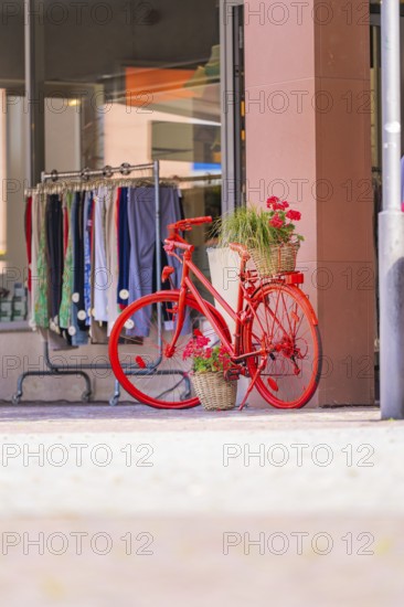 Bright red bicycle with flower arrangement in front of a fashion shop in a sunny street, small town Perle Calw, Black Forest, Germany
