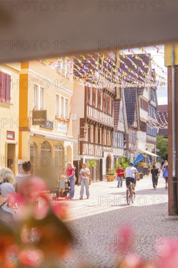 Passers-by and a cyclist in a lively old town street with traditional houses and shops, small town of Perle Calw, Black Forest, Germany
