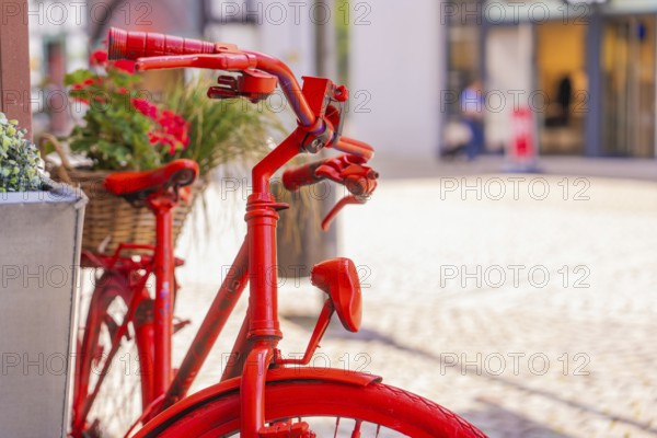 Close-up of a red bicycle handlebar with flower baskets in a lively city scene, small town of Perle Calw, Black Forest, Germany