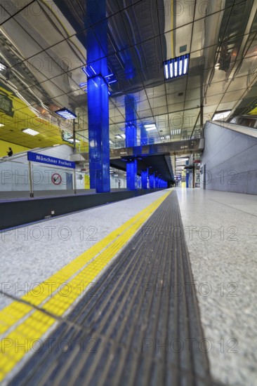 Modern underground station with blue light columns and yellow floor markings, Munich, Germany