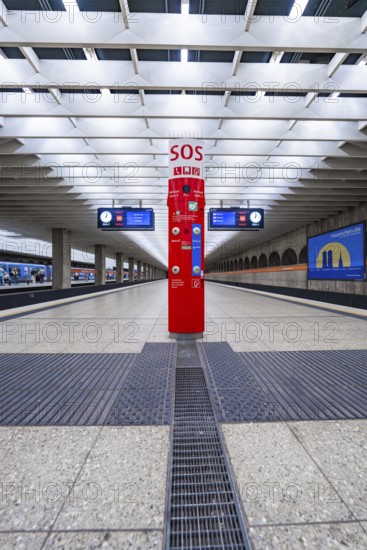 A central SOS pillar in a modern railway station concourse with empty platforms, Munich, Germany