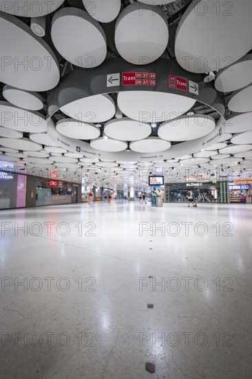 Spacious underground station with modern ceiling and lights, few people scattered around, Munich, Germany