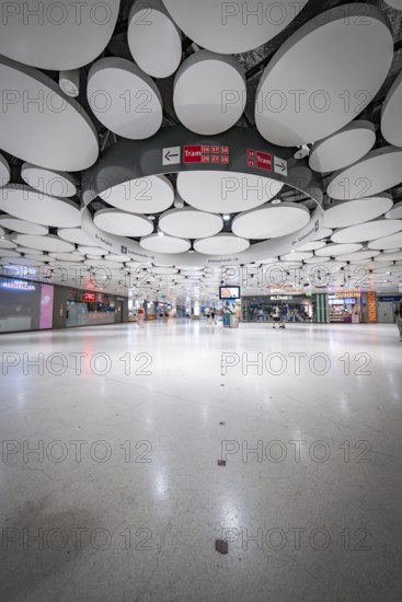 Spacious underground station with modern ceiling and lights, some people scattered in the room, Munich, Germany