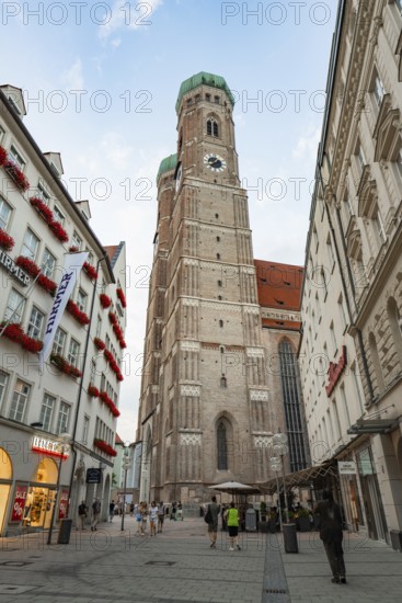 High bell tower of a church surrounded by historical buildings and people on a square, Munich, Germany