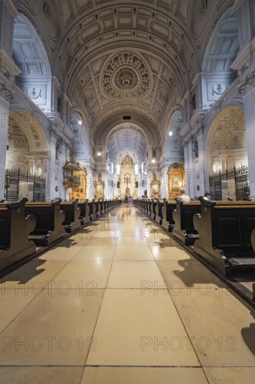 Magnificent church interior with long wooden benches, ornate altar and impressive dome, Munich, Germany