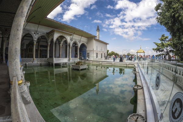 Tourists walking around the courtyard with reflecting pool of the topkapi palace in istanbul, turkey, on a sunny day