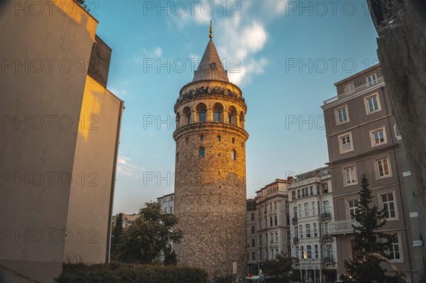 Galata tower, a medieval stone tower, is illuminated by the setting sun in istanbul, turkey, surrounded by buildings and a vibrant sky