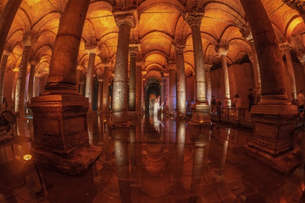 Tourists walking on a walkway in the basilica cistern in istanbul, turkey, with warm light reflecting on columns and water