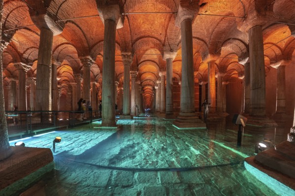 Tourists walking on a walkway in the basilica cistern, a historical landmark in istanbul, turkey, with turquoise illuminated water and ancient columns