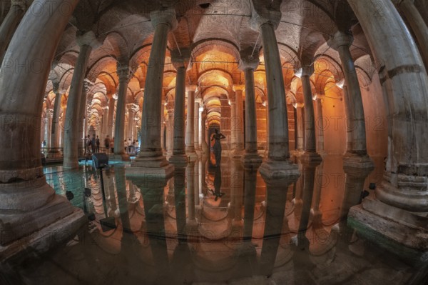 Ancient underground basilica cistern reflecting on water surface with tourists and medusa head sculpture in istanbul, turkey