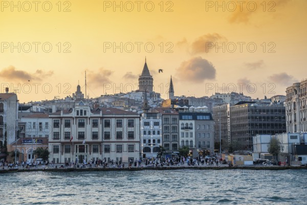 Tourists enjoying sunset view of galata tower and cityscape of istanbul, turkey, from the bosphorus strait with golden light illuminating buildings and cloudy sky