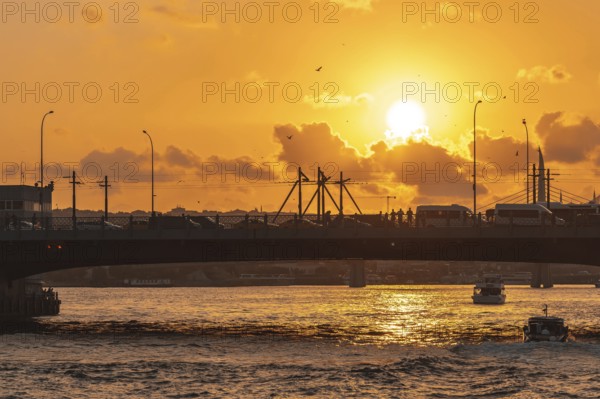 The golden horn waterway in istanbul, turkey, glows under a vibrant sunset, with a bridge full of commuters and boats navigating the waters