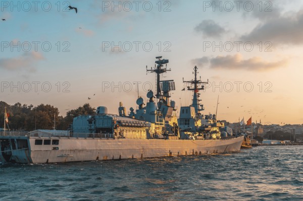 Modern warship gliding through the tranquil sea near istanbul, turkey, under a stunning golden hour sky filled with warm hues