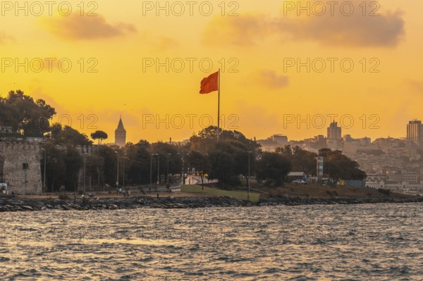 Scenic sunset view of istanbul's cityscape, featuring the prominent galata tower and a waving turkish flag, creating a patriotic and picturesque scene