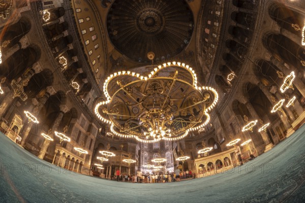 Fisheye view of tourists visiting the magnificent interior of hagia sophia, showcasing its stunning architecture, intricate mosaics, and impressive chandeliers