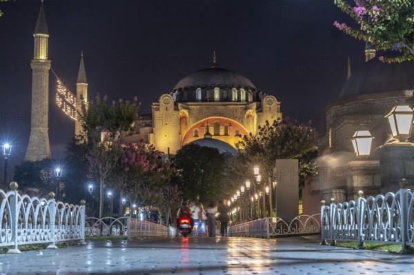 Tourists strolling in front of the hagia sophia mosque, beautifully illuminated at night, creating a stunning scene in istanbul, turkey