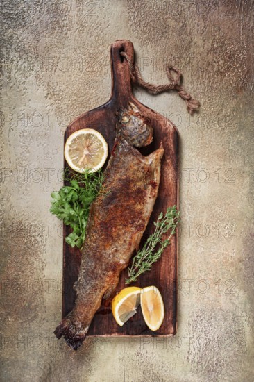 Fried rainbow trout, with herbs and citrus fruits, on a wooden chopping board, top view