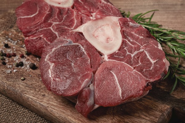 Knuckle on the bone, raw meat for ossobuco, on a wooden chopping board, with a sprig of rosemary, and spices, top view, no people