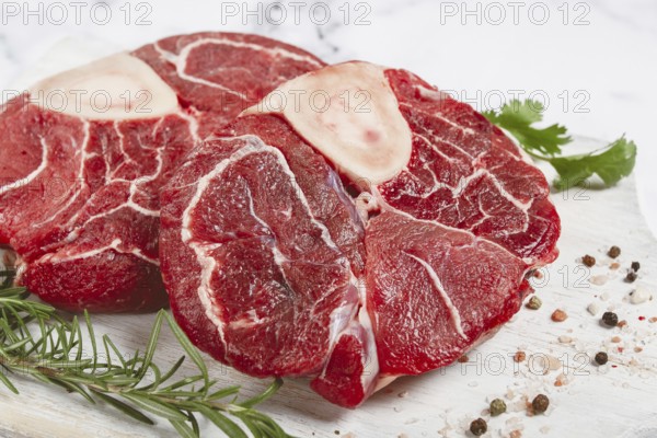 Knuckle on the bone, raw meat for ossobuco, on a wooden chopping board, with a sprig of rosemary, and spices, top view, no people