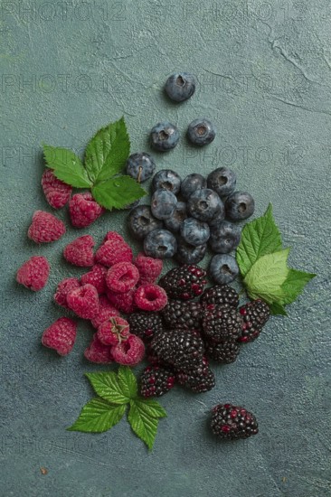 A mix of ripe berries, with leaves scattered on the table, raspberries, blackberries, blueberries, food background