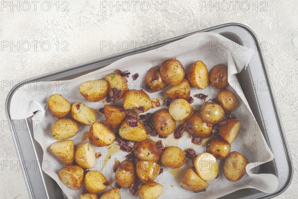 Golden-brown roasted potatoes are arranged on a baking tray lined with parchment paper. They are seasoned with herbs and garnished with crispy bacon bits, ready to be enjoyed