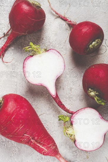 Bright red radishes are arranged on a counter, with one radish cut in half to reveal the crisp white interior. The green tops add a touch of freshness to the composition