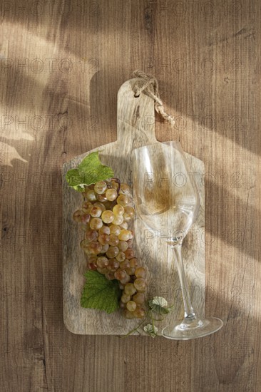 A sprig of white grapes, on a wooden board, with a glass of white wine, top view, natural lighting, food concept, no people
