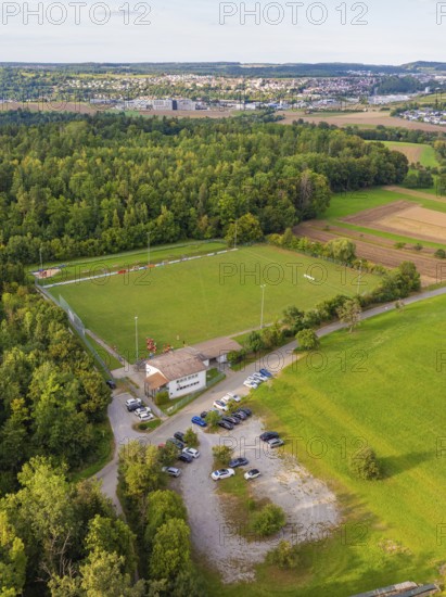 Aerial view of a sports field in the middle of wooded and rural surroundings with parked cars and a view of a village, VFL Stammheim, Calw, Black Forest, Germany