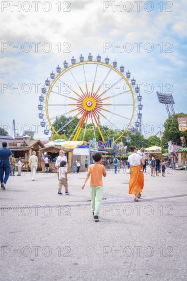 People on a square in an amusement park with a large Ferris wheel in the background, Olympiapark, Munich, Germany
