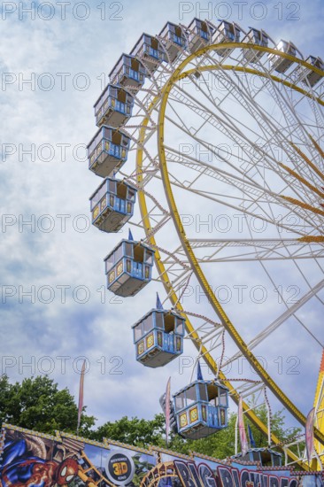 A large section of a Ferris wheel with numerous cabins above a fairground attraction, Olympiapark, Munich, Germany