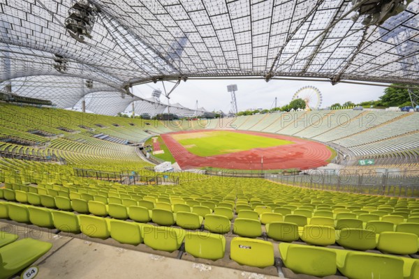 Overview of the stadium with green seats and red running track, framed by an impressive roof design, Olympiapark, Munich, Germany