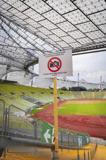View of stadium grandstand and running track, dominated by a metal grid construction and prohibition sign in the foreground, Olympiapark, Munich, Germany