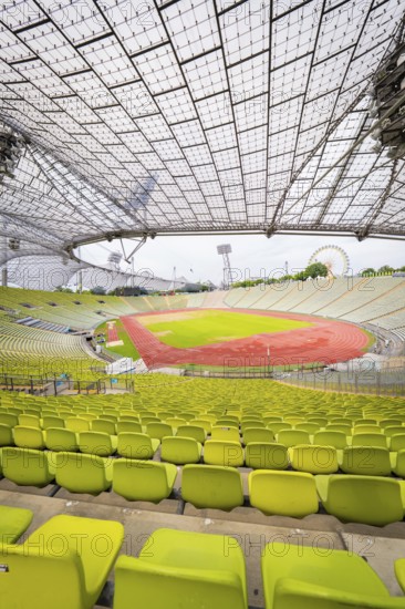 Panoramic view of stadium with yellow-green seats and red running track under a filigree roof, Olympic Park, Munich, Germany