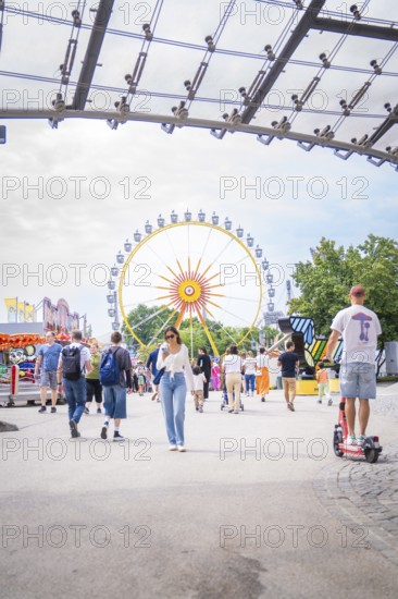 People in amusement park with e-scooter and big Ferris wheel in the background, Olympiapark, Munich, Germany