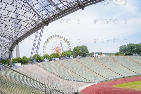 Open stadium with a view of a Ferris wheel in the background and green rows of seats, Olympic Park, Munich, Germany