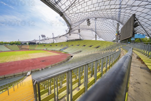 Empty modern stadium with green seats and striking glass roof under a blue sky, Olympiapark, Munich, Germany