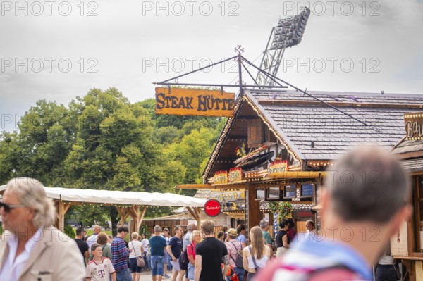 A traditional building with a crowd in front of it, surrounded by nature and advertising, Olympiapark, Munich, Germany