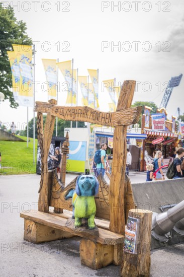 Wooden bench with colourful bear figure and lettering in amusement park with background of visitors, Olympic Park, Munich, Germany