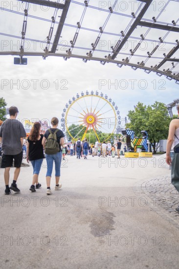 View of a Ferris wheel in an amusement park through a modern construction with many visitors, Olympic Park, Munich, Germany