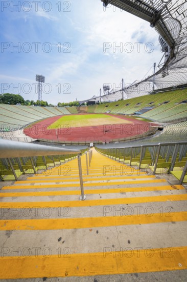 View down the yellow steps to an empty stadium with wide stands and running track, Olympiapark, Munich, Germany